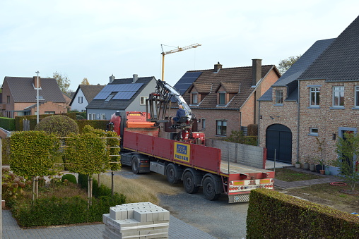 Leuven, Vlaams-Brabant, Belgium - October 28, 2022: truck driver seen from his back sitting on a hydraulic lifting crane on the truck manipulating cargo