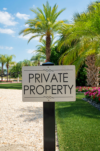 Destin, Florida- Sign on a post with Private Property outdoors. Signage against the view of white gravel on the left and landscaped grass, plants, and trees on the right.