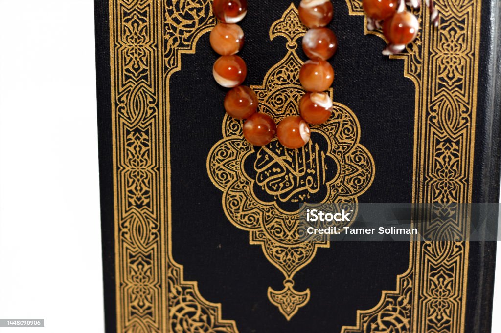 The holy Quran, Qur'an or Koran (the recitation) is the central religious text of Islam, believed by Muslims to be a revelation from God (Allah), isolated on white background with a rosary on it The holy Quran, Qur'an or Koran (the recitation) is the central religious text of Islam, believed by Muslims to be a revelation from God (Allah), isolated on white background with a rosary on it, selective focus Allah Stock Photo