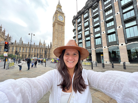 She poses in front of Big Ben clock tower, fun exploring the city, solo travel concept