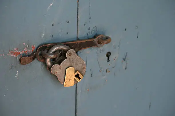 Old doorlock locks an old blue door. This door is secured (keys).