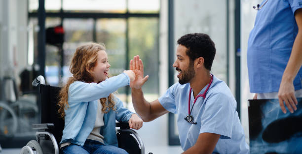 Young multiracial doctor having fun with little girl on wheelchair. stock photo
