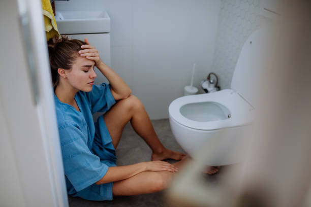 Young sick woman sitting on floor near toilet. stock photo