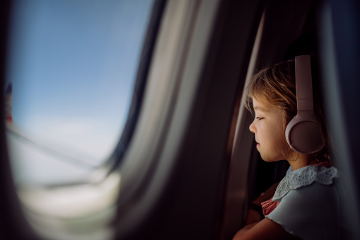 Little girl in airplane listening music and looking out of the window.