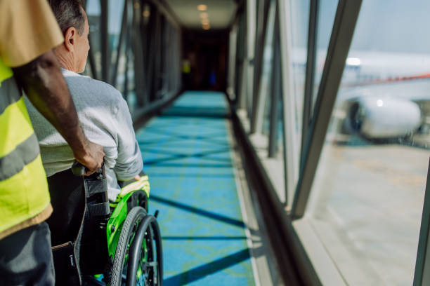 Rear view of airport worker pushing man on wheelchair in the airplane. Concept of traveling with special needs. stock photo