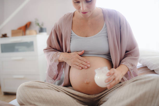 Pregnant woman creaming her belly, taking care of herself. Pregnant woman creaming her belly,sitting in a bed, taking care of herself. creaming stock pictures, royalty-free photos & images