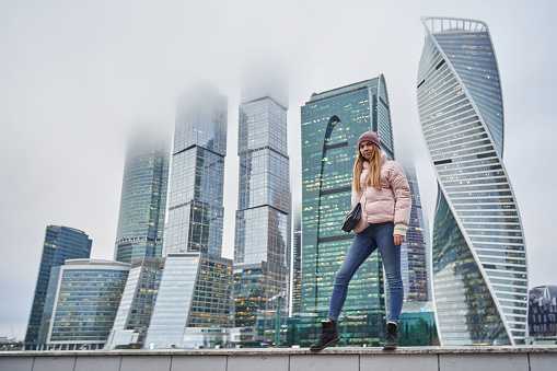 beautiful young woman next to skyscrapers and skyscrapers of a big city. tall business centers in the clouds in the background. High quality photo