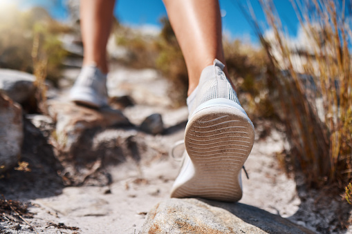 Shoes, hiking and fitness with a woman closeup walking up a mountain trail for exercise, cardio or adventure. Nature, training and feet with a female hiker stepping on a rock while outdoor for a walk