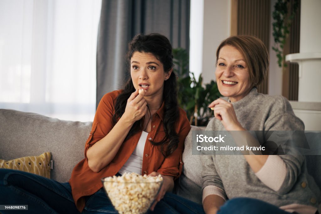 Mother and daughter watching movie together and eating pop corns Reality TV Stock Photo