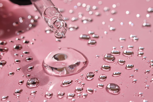 Pipette, drop and splashes of micellar water on a pink background.