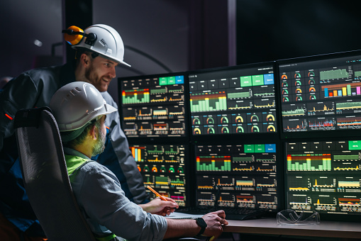 Head engineer and factory operator following product process on factory uses SCADA system and industry 4.0. Two operators controll assembly line using screens with human-machine interface