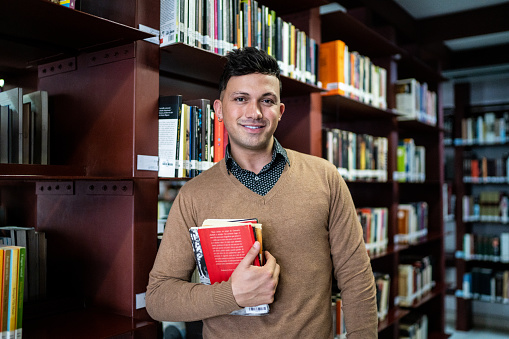 Portrait of a young man holding a book in a library