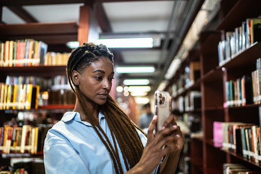 Young woman scanning book using mobile phone in the library