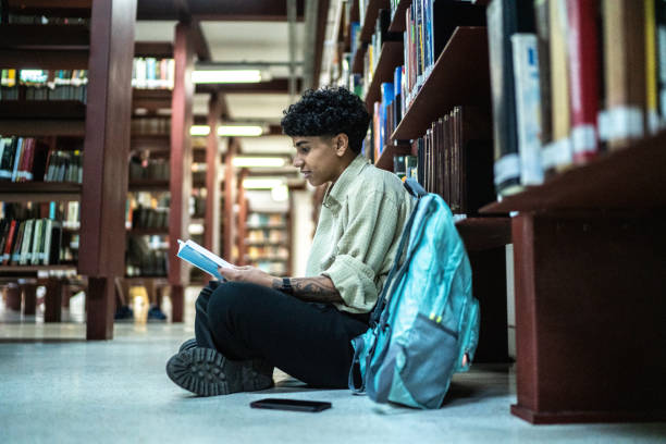 istock Young woman reading a book in the library 1448116992