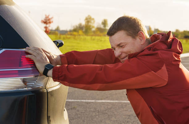 mężczyzna pcha swój zepsuty samochód na parking. - heat effort emotional stress business zdjęcia i obrazy z banku zdjęć