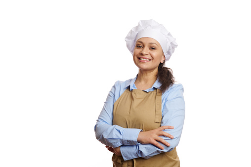 Cheerful female baker confectioner, pastry chef, female cook, waitress in chef's hat and apron, smiling a cheerful toothy smile looking at camera, isolated on white background. Copy advertising space