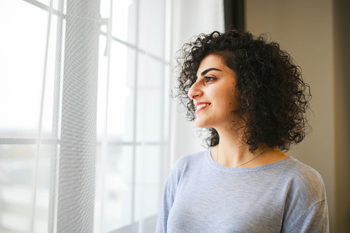 portrait of smiling brunette woman with curly hair in front of window