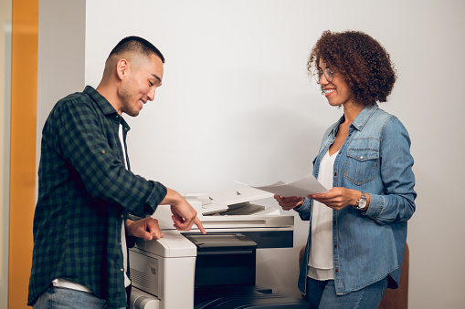Joyous office worker pointing his index finger at the photocopier to a smiling female secretary