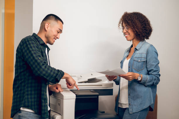 Corporate workers making photocopies on the copy machine Joyous office worker pointing his index finger at the photocopier to a smiling female secretary photocopier stock pictures, royalty-free photos & images