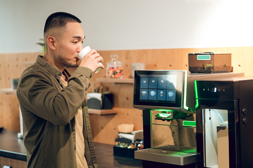 Corporate worker standing before the coffee machine and drinking a beverage from a disposable paper cup