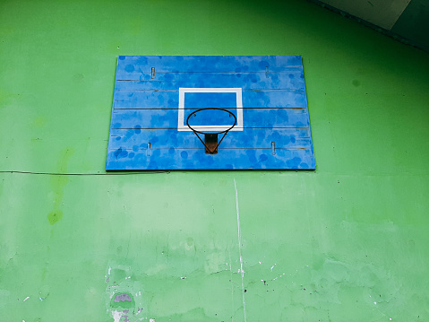 A basketball hoop that uses a wooden plank in blue color against a green wall