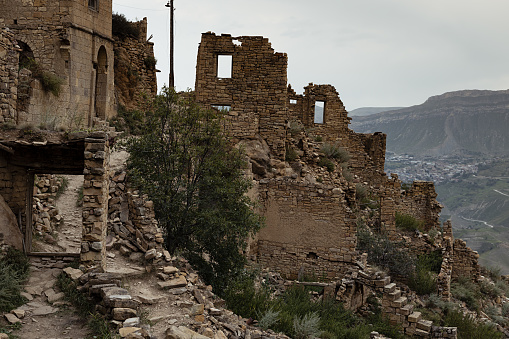 Ruin of old stone town on peak of in Caucasian mountains in Dagestan, fragments of destruction houses, street in medieval stone city in highlands in overcast. Archeology adventure and tourist trip.