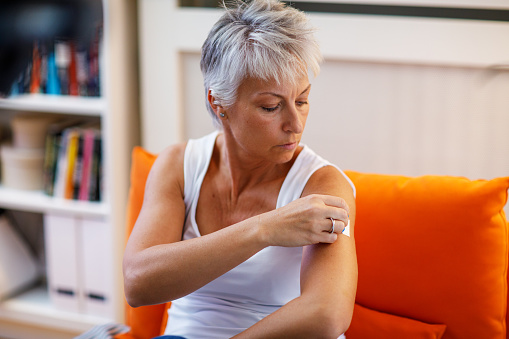 A woman in menopause sticks a transdermal patch on the skin. Hormone replacement therapy in menopause concept.