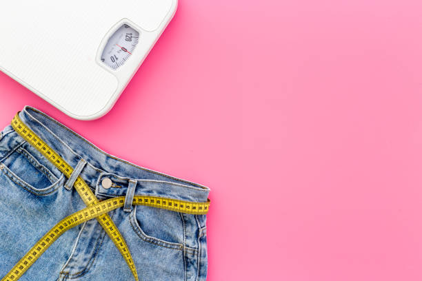Jeans with measuring tape belt and scales. Weight loss and diet concept stock photo