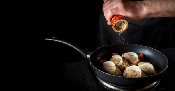 istock Cooking cutlets on pan by chef hands on black background for copy space text restaurant menu. The chef or cook adds pepper 1448125278