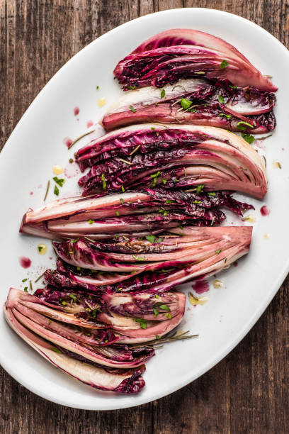 radicchio salad (radicchio rosso di treviso, veneto) stewed in red wine and aromatic herbs on in an old rustic plate, rustic wooden background. winter recipes from the north italy, close-up - salad food and drink food lettuce imagens e fotografias de stock