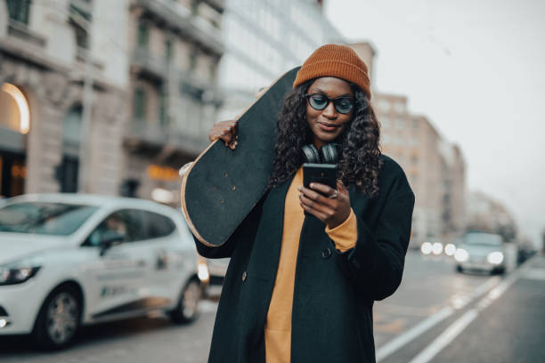 A young black woman, hipster style, with a skateboard in her hands walks down the street of Barcelona stock photo