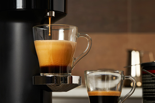 Closeup of a glass cup with fresh coffee from a capsule coffee machine against the backdrop of a home kitchen. Selective focus.