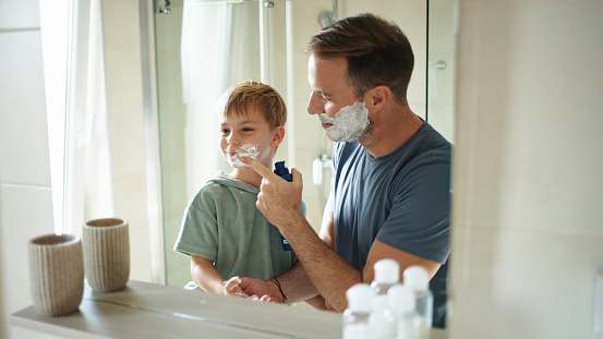 A father teaching his little son how to shave in the bathroom at home
