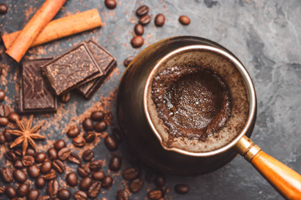 Fresh brewed coffee in the turkish jezva coffee pot on dark background with coffee beans and chocolate pieces, top view Fresh brewed coffee in the turkish jezva coffee pot on dark background with coffee beans and chocolate pieces, top view. cezve stock pictures, royalty-free photos & images