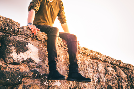 low section of a man sitting on a brick wall in a sunny day