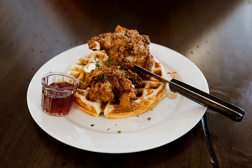 A plate of fried chicken strips and waffles and maple syrup.