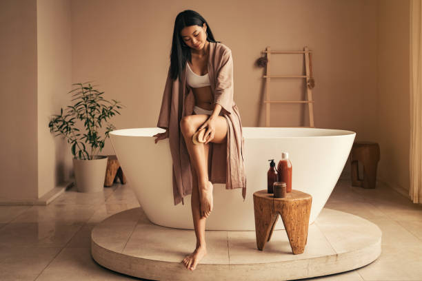 皮むき手順を行うアジアの若い女性、浴室で木製のブラシで乾式ブラッシング