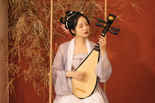 An Asian beauty plays the pipa on the swing