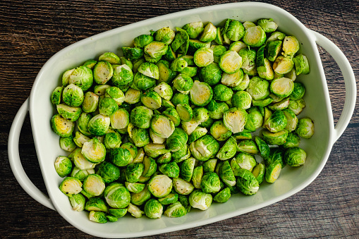 A baking dish full of raw Brussels sprouts cut in half and tossed in olive oil, salt and pepper