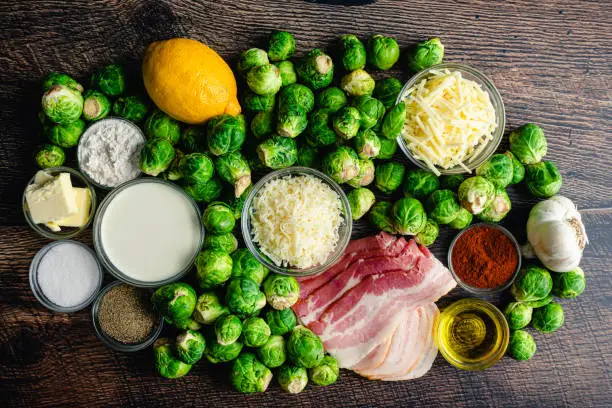 Overhead view of fresh Brussels sprouts, bacon, cheese, and other raw ingredients