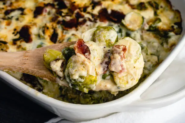 A wooden spoon holding Brussels sprouts cooked in cream and cheese sauce