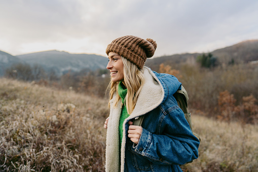 Photo of a young woman hiking with a backpack through beautiful nature on a chilly autumn day.