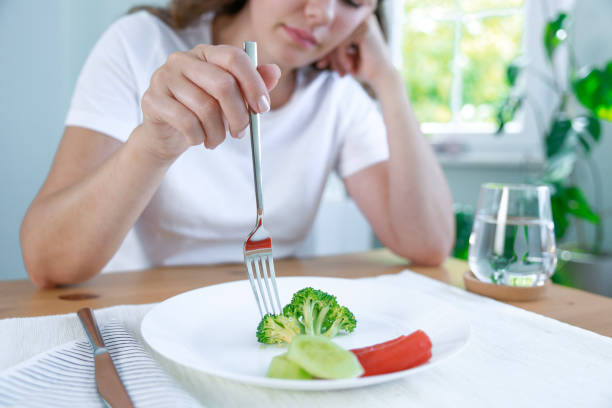 First day of diet. Unhappy young woman looking at small broccoli portion on the plate stock photo