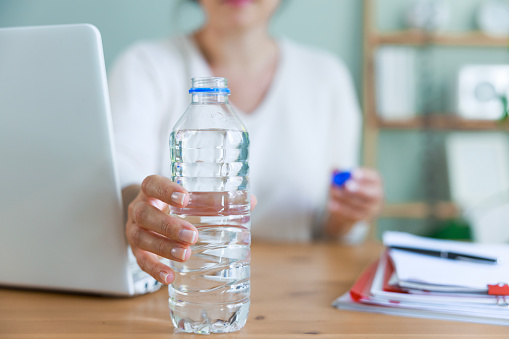 Young woman reaching for bottle of water as she takes a break from using laptop. Concept of the importance of drinking water