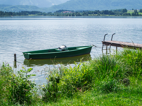 Landscape view on the shore of the Hopfensee in Bavaria with the Ange rowing boat in the foreground on the jetty and the first foothills of the German Alps.