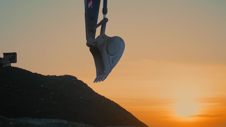 Low angle view of excavator flipping the bucket with soil at sunset