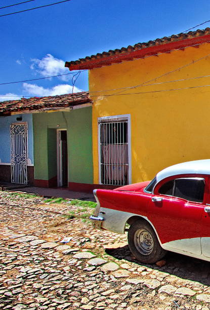 Part of a vintage car in front of multicolored buildings on a cobblestone street in Trinidad, Cuba stock photo