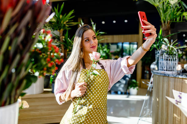 młoda piękna kobieta używa telefonu do zrobienia zdjęcia selfie w kwiaciarni. - spring nature life events arrangement zdjęcia i obrazy z banku zdjęć