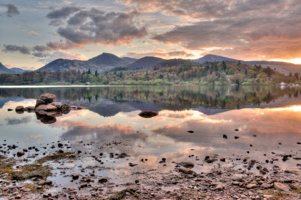 An old jetty on the still water of Derwent Water in Cumbria with the sun shining on the hills in the distance.