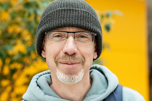 Close-up portrait of a happy 50 year old white bearded man with glasses in a hooded shirt and a knitted hat